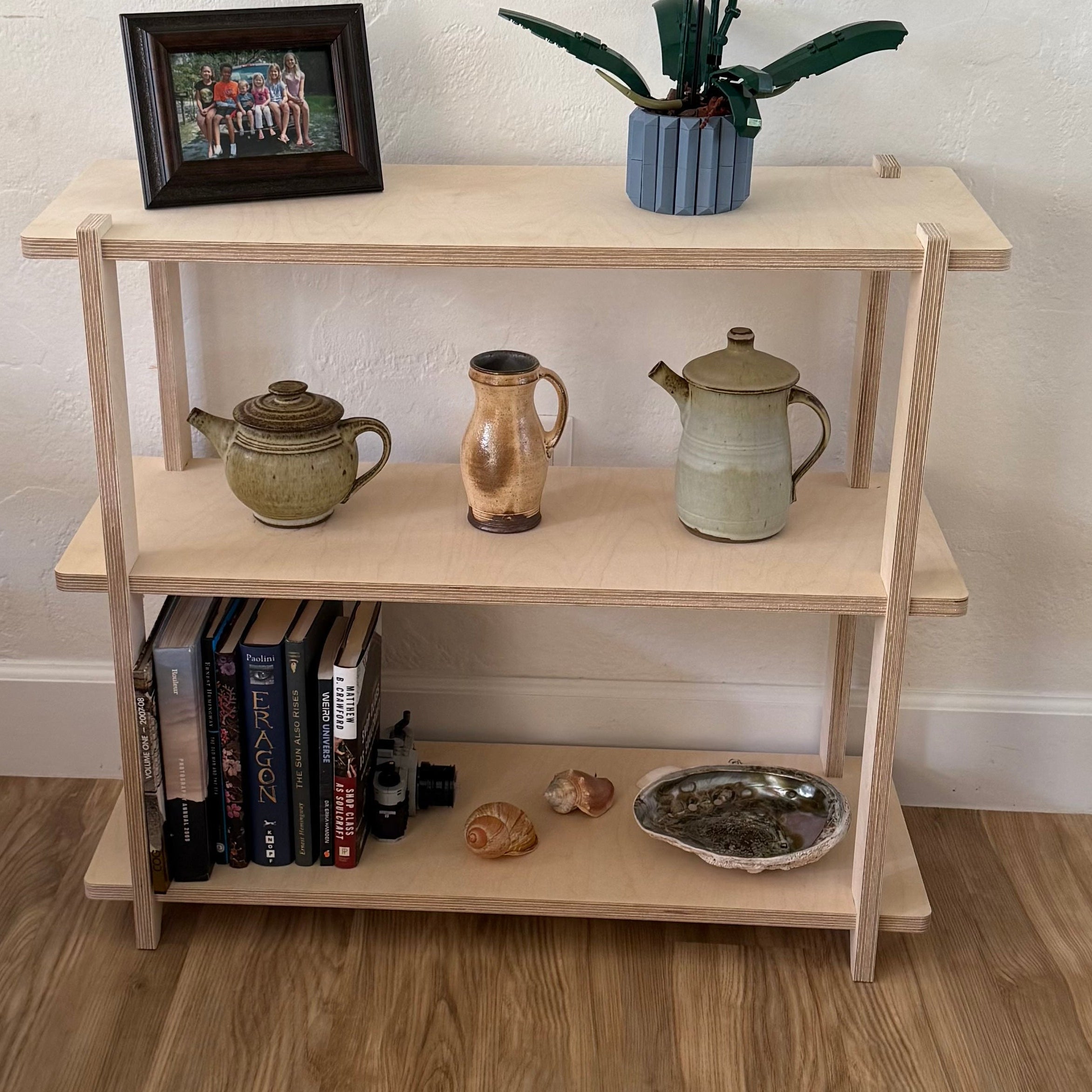 Wooden shelf with decorative items including books, teapots, and a vase on a wooden floor.
