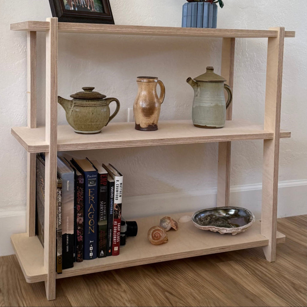 Wooden bookshelf with decorative items including books, teapots, and a vase on a wooden floor.